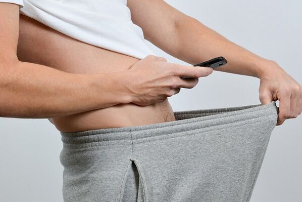 un homme regarde dans son pantalon un pénis agrandi